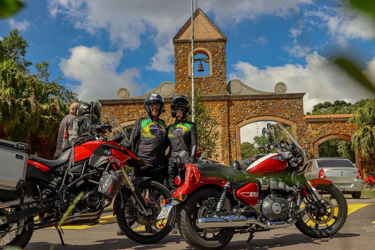 Parada de viagem diante de um portal de pedra, com motociclistas e suas motos